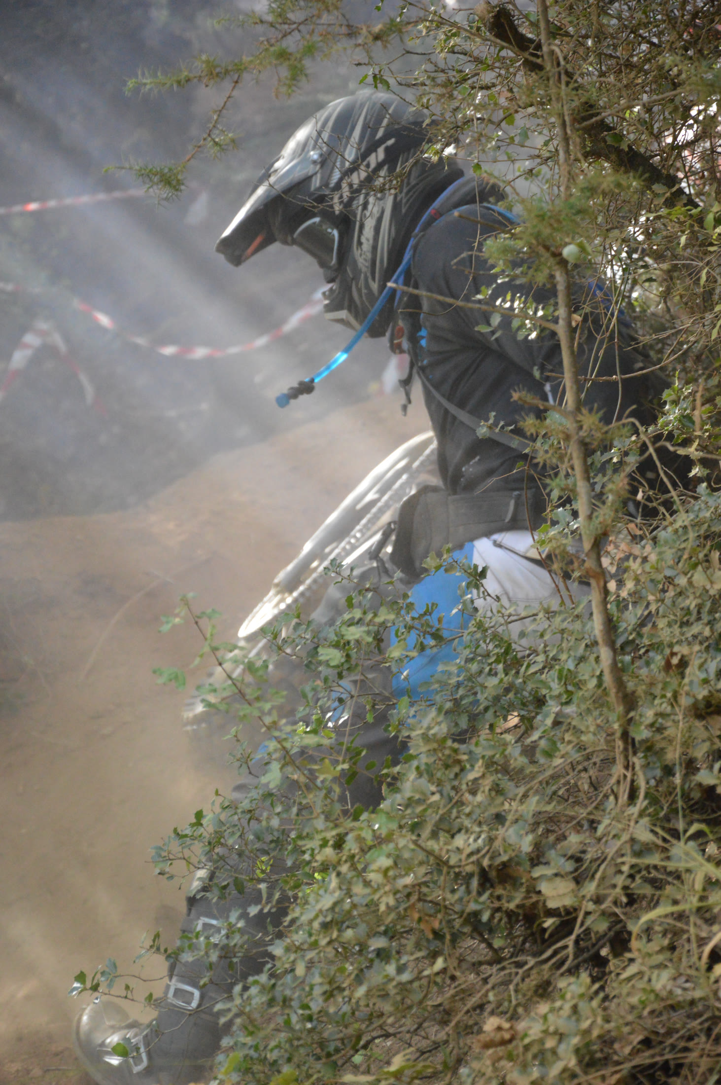 Off-road motorcycle rider moving through dust and dense mountain vegetation